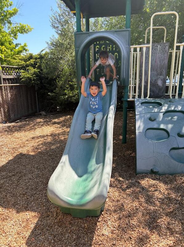 A child cheering on the way down the playground slide
