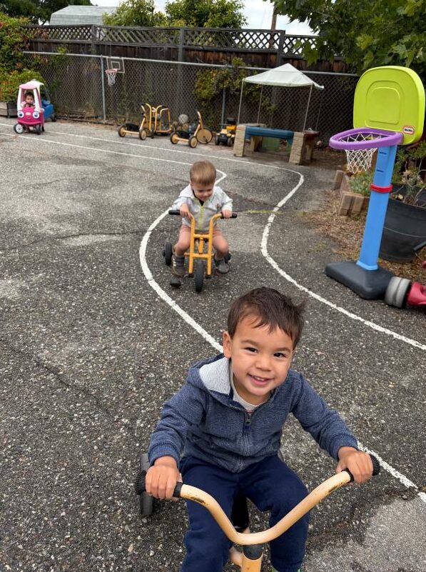 A smiling boy riding a trike on the playground track