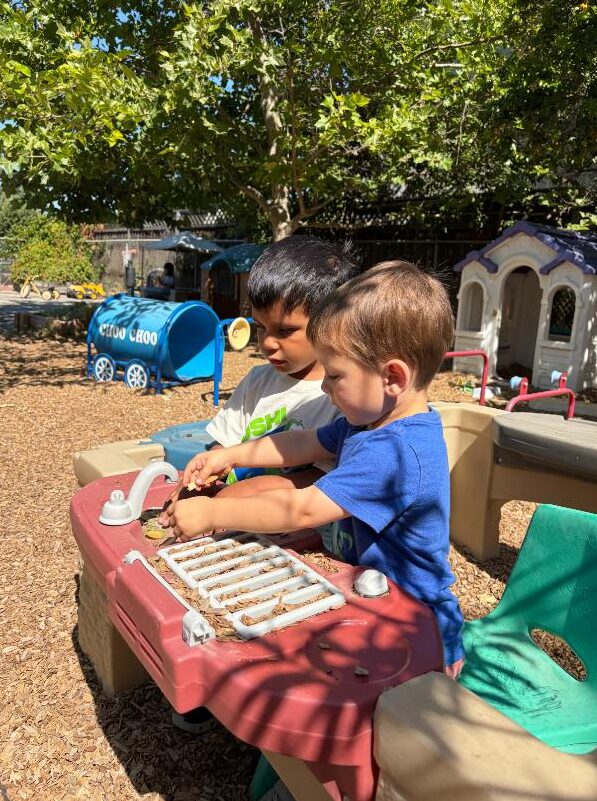 Two children playing side by side at the outdoor play kitchen