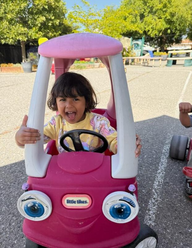 A toddler laughing in a ride-on car on the playground