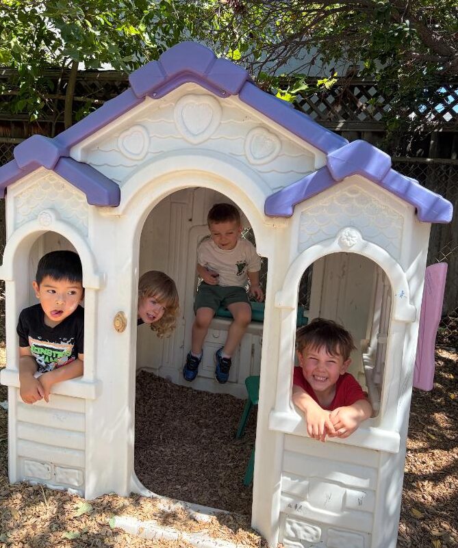 Four children smiling from the windows of the outdoor playhouse