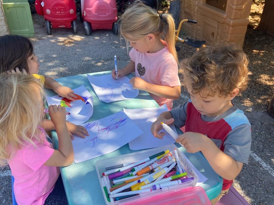 Children drawing and writing with markers outdoors