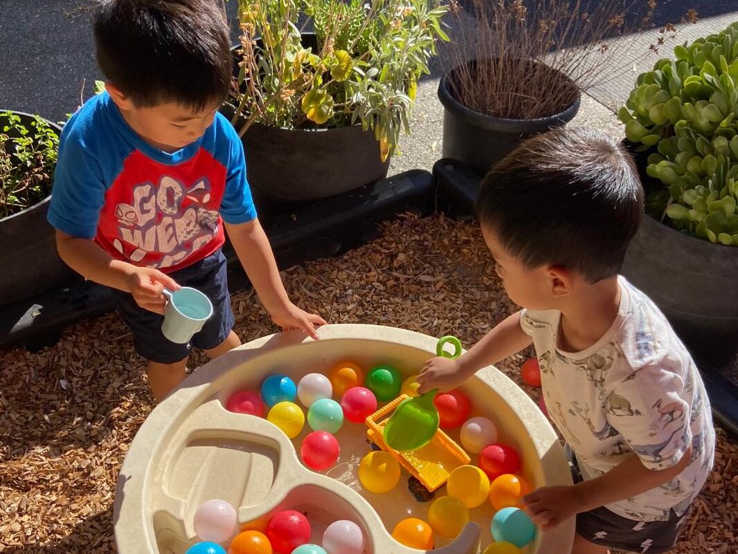 Two children scooping and pouring at the water table