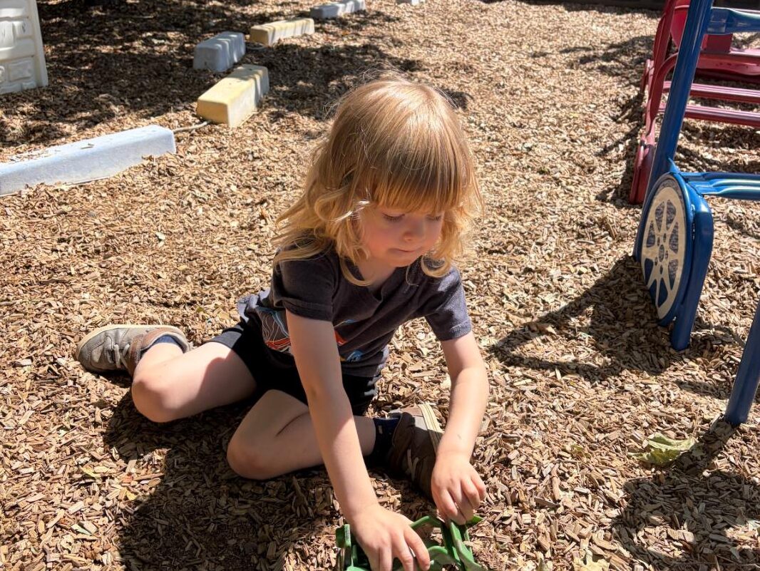 A child playing independently with a toy truck outdoors