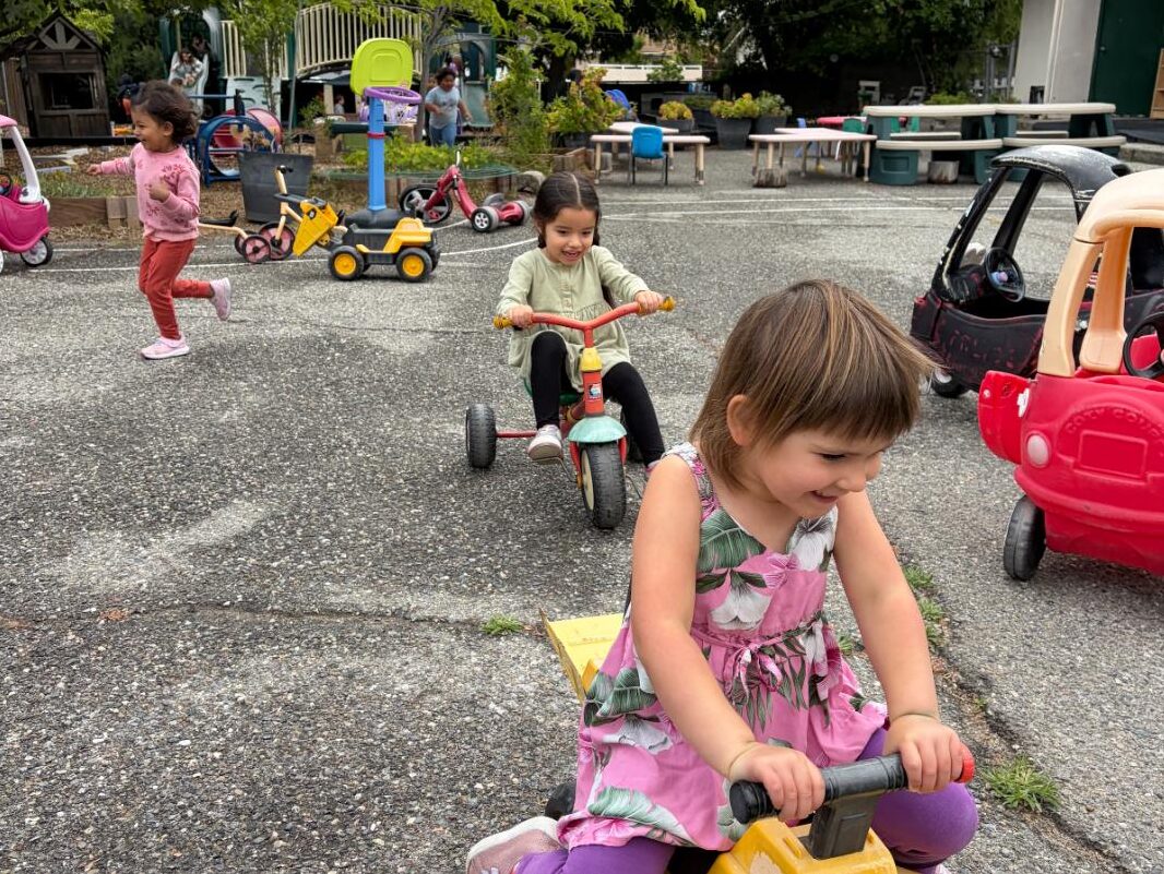 Children taking turns on ride-on toys in the play yard