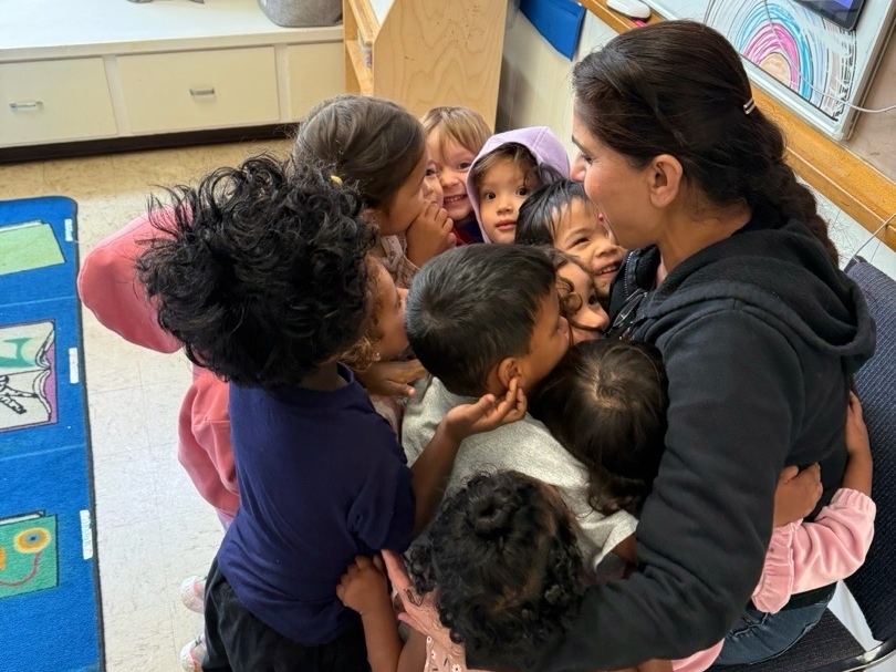 An ECLA teacher sharing a group hug with children