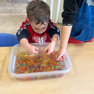 A child exploring a sensory tray of water beads