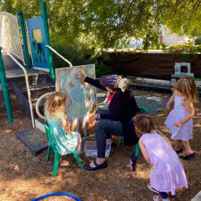 A teacher and children painting at the outdoor easel