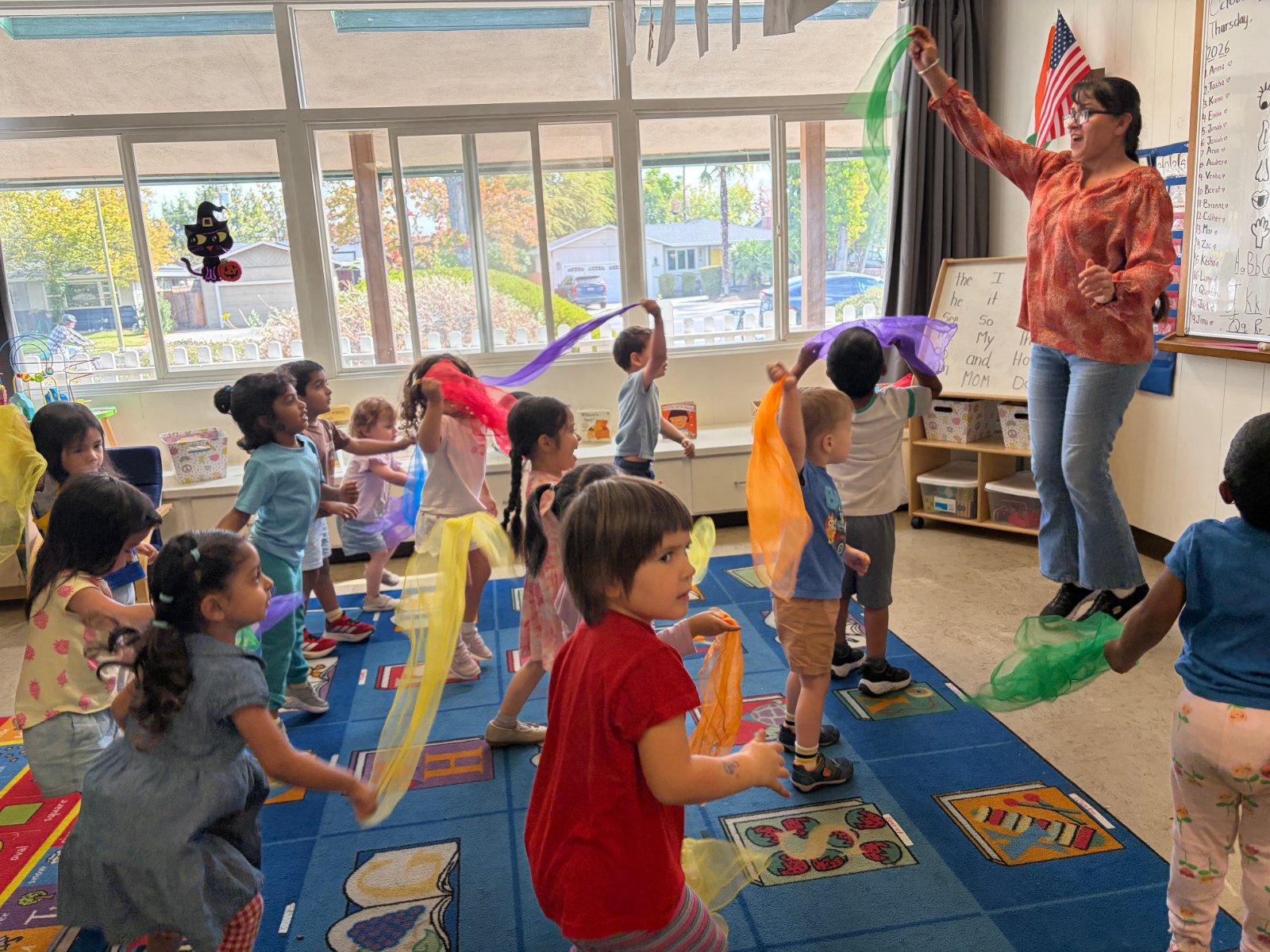 Children dancing with colorful scarves during music time with their teacher